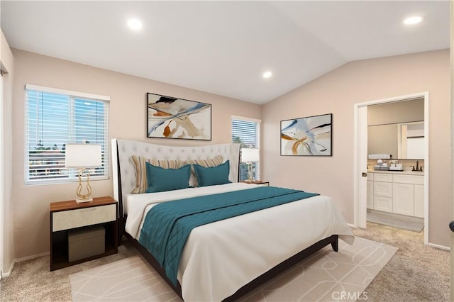 bedroom featuring lofted ceiling, light colored carpet, and ensuite bath