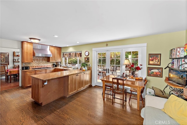 kitchen with stainless steel gas stovetop, backsplash, dark hardwood / wood-style flooring, kitchen peninsula, and wall chimney exhaust hood