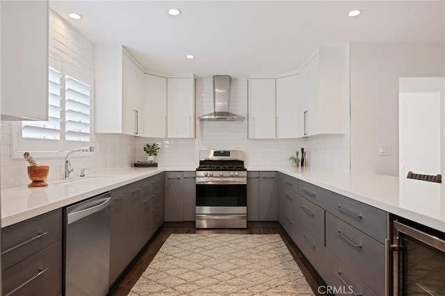 kitchen with wall chimney exhaust hood, sink, white cabinetry, appliances with stainless steel finishes, and beverage cooler