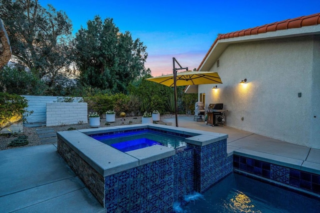 pool at dusk featuring an in ground hot tub and a patio area