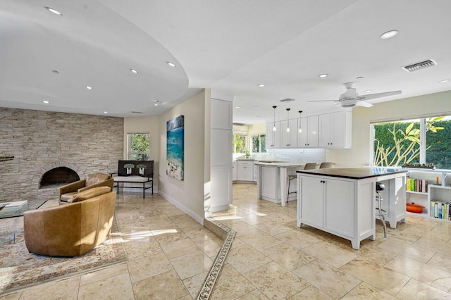 kitchen featuring a stone fireplace, a breakfast bar, decorative light fixtures, a kitchen island, and white cabinets