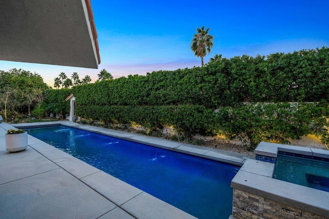 pool at dusk with pool water feature and an in ground hot tub