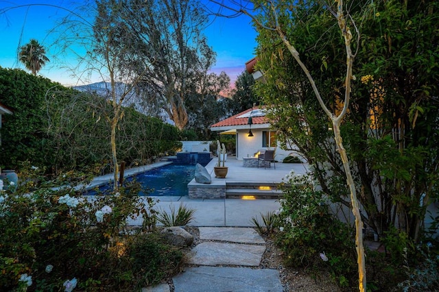 pool at dusk featuring a jacuzzi and a patio area