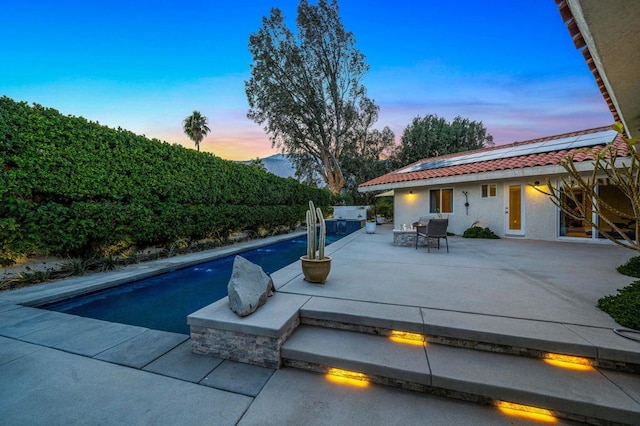 pool at dusk featuring exterior kitchen and a patio