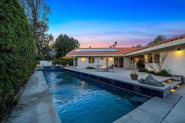 pool at dusk featuring pool water feature, a patio area, and an outdoor fire pit