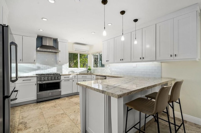 kitchen with white cabinetry, premium appliances, kitchen peninsula, a wall unit AC, and wall chimney range hood