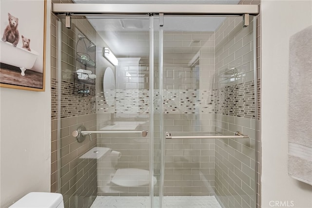 bathroom featuring a shower with door and toilet