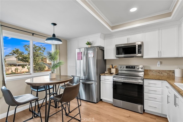 kitchen featuring decorative light fixtures, ornamental molding, a tray ceiling, stainless steel appliances, and white cabinets