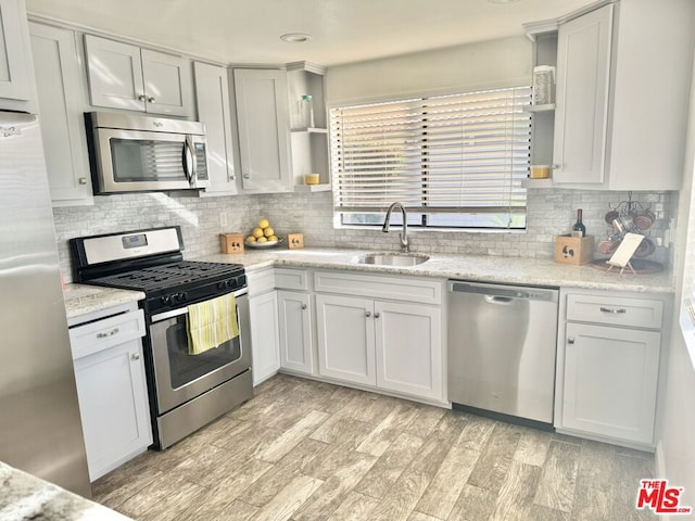 kitchen with light stone counters, sink, light hardwood / wood-style flooring, and appliances with stainless steel finishes