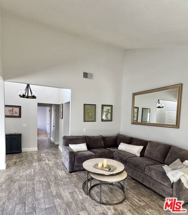 living room featuring wood-type flooring, a chandelier, and high vaulted ceiling