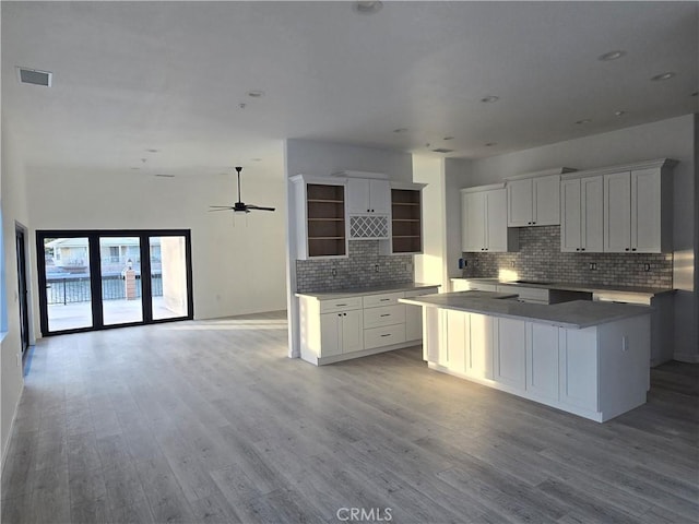 kitchen with tasteful backsplash, white cabinetry, a kitchen island, and light hardwood / wood-style flooring