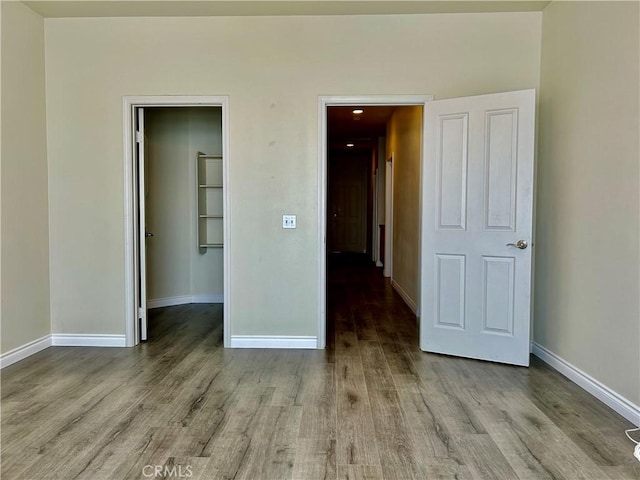 unfurnished bedroom featuring a walk in closet, baseboards, and wood finished floors