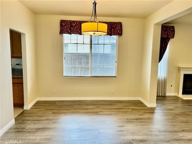 unfurnished dining area featuring a fireplace with raised hearth, wood finished floors, and baseboards