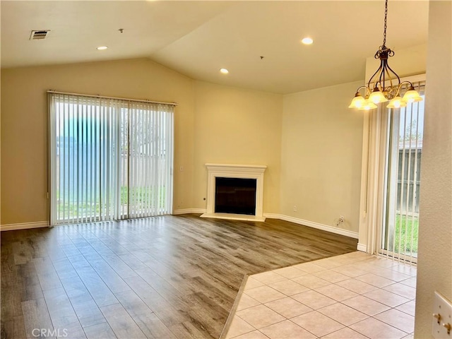 unfurnished living room with lofted ceiling, a fireplace with raised hearth, plenty of natural light, and visible vents