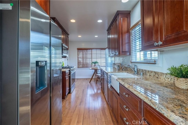 kitchen with stainless steel appliances, sink, light stone counters, and light wood-type flooring