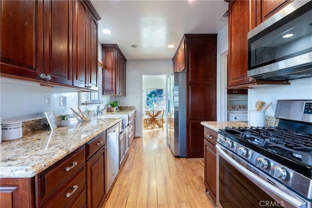 kitchen with light stone counters, stainless steel appliances, sink, and light hardwood / wood-style flooring