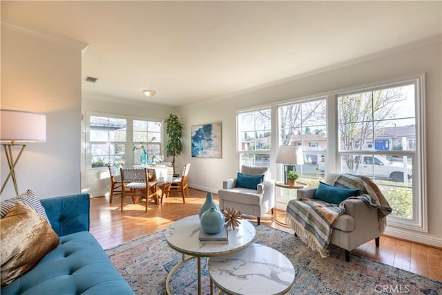 living room featuring crown molding, a healthy amount of sunlight, and light wood-type flooring