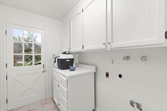 clothes washing area with electric dryer hookup, light tile patterned floors, and cabinets