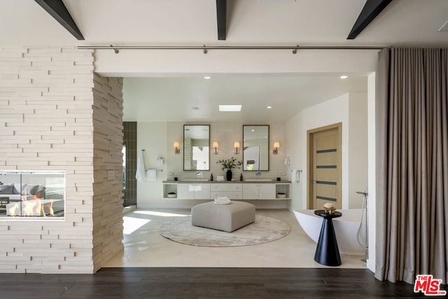 bathroom featuring hardwood / wood-style floors, a multi sided fireplace, vanity, a tub to relax in, and beamed ceiling