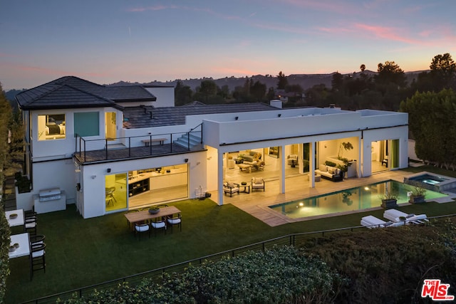 back house at dusk featuring a yard, a patio area, outdoor lounge area, and a balcony