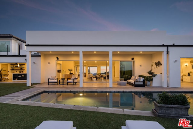 back house at dusk with a balcony, outdoor lounge area, a yard, and a patio area