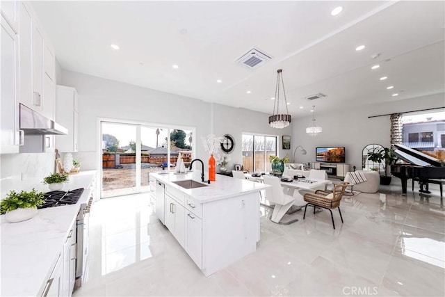 kitchen featuring pendant lighting, white cabinetry, an island with sink, sink, and light stone countertops