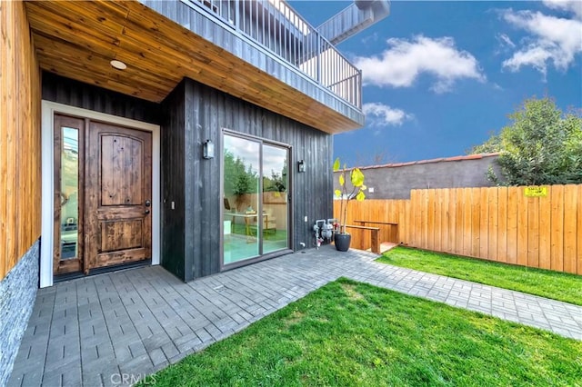 property entrance with a balcony, a patio area, and a lawn