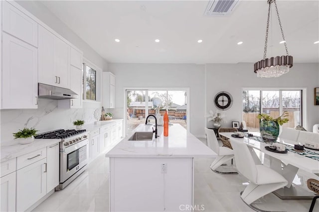 kitchen featuring an island with sink, white cabinetry, sink, hanging light fixtures, and stainless steel range