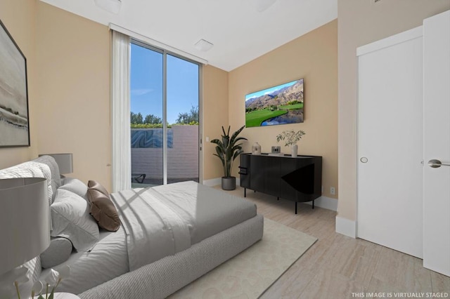 bedroom featuring a wall of windows, light hardwood / wood-style flooring, and access to outside