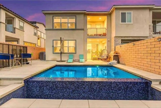 back house at dusk featuring a fenced in pool and a patio area