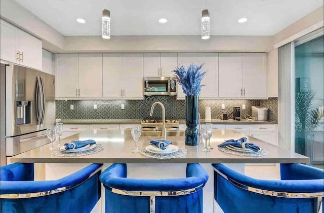 kitchen featuring white cabinetry, appliances with stainless steel finishes, an island with sink, and decorative light fixtures