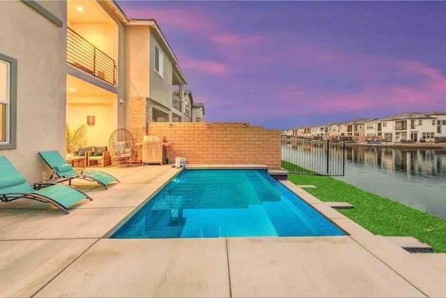 pool at dusk with a patio area and a water view