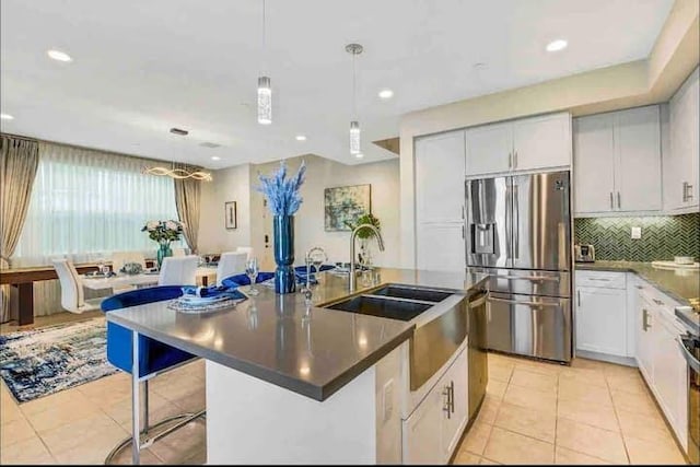 kitchen with stainless steel refrigerator with ice dispenser, light tile patterned flooring, decorative light fixtures, a center island with sink, and white cabinets