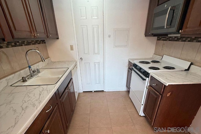 kitchen with tasteful backsplash, sink, light tile patterned floors, dark brown cabinets, and white appliances