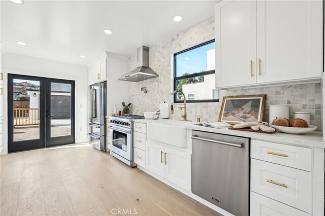 kitchen featuring sink, white cabinets, high end appliances, light wood-type flooring, and wall chimney exhaust hood