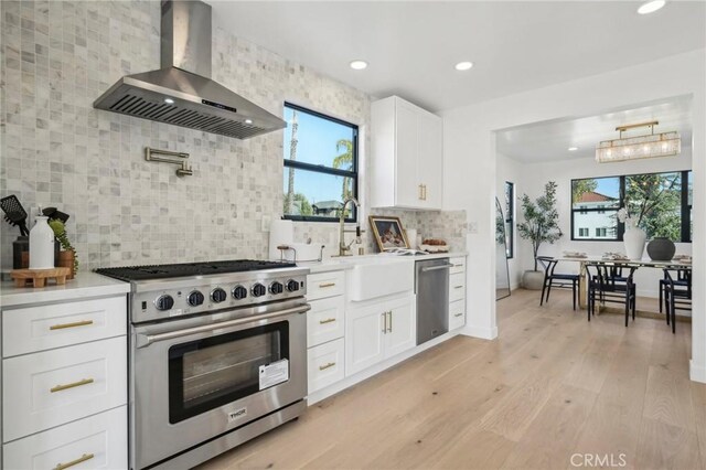 kitchen with wall chimney exhaust hood, sink, light wood-type flooring, stainless steel appliances, and white cabinets