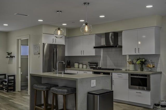 kitchen featuring sink, appliances with stainless steel finishes, pendant lighting, wall chimney range hood, and white cabinets