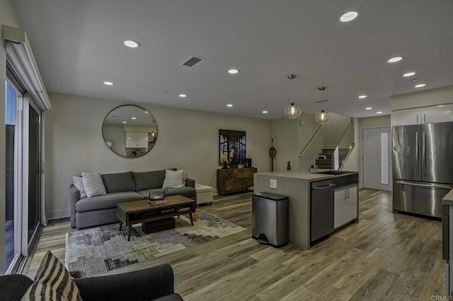 kitchen with sink, appliances with stainless steel finishes, hanging light fixtures, wood-type flooring, and an island with sink