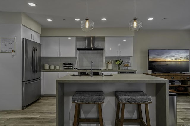 kitchen featuring white cabinetry, black fridge, pendant lighting, and wall chimney exhaust hood