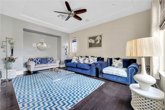 living room with dark wood-type flooring, ceiling fan, and a tray ceiling