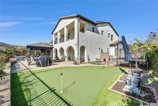 back of property with an outdoor fireplace, a gazebo, a balcony, and a patio area