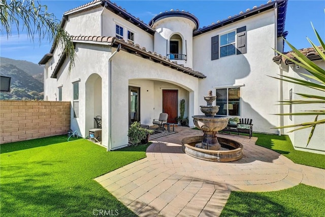 back of property featuring a balcony, a yard, a mountain view, and a patio area