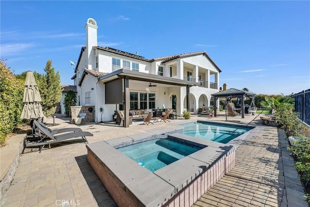 rear view of house with a swimming pool with hot tub, ceiling fan, a gazebo, a patio, and a balcony