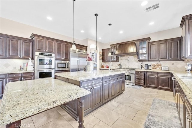 kitchen with pendant lighting, a center island, built in appliances, light stone countertops, and custom exhaust hood