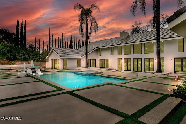 pool at dusk featuring a patio and an in ground hot tub