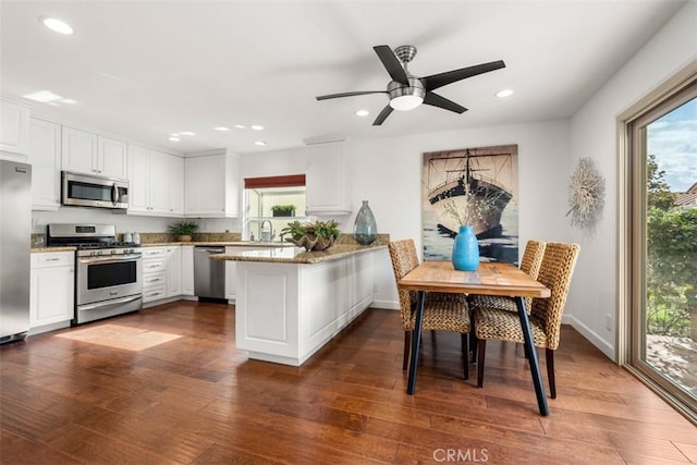 kitchen with stainless steel appliances, light stone counters, white cabinets, dark hardwood / wood-style flooring, and kitchen peninsula