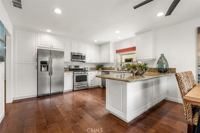 kitchen featuring stainless steel appliances, light stone counters, white cabinets, dark hardwood / wood-style flooring, and kitchen peninsula