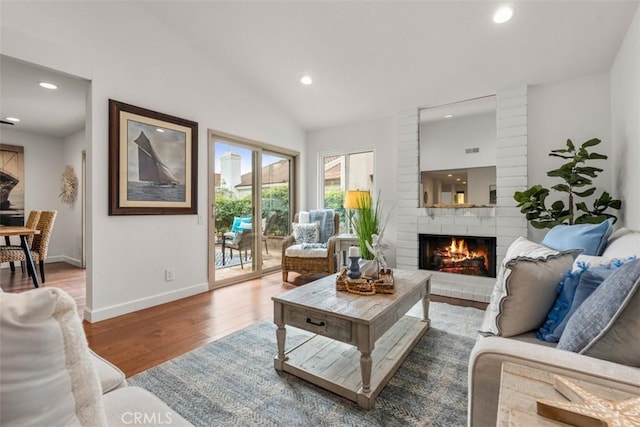 living room featuring hardwood / wood-style flooring, lofted ceiling, and a brick fireplace