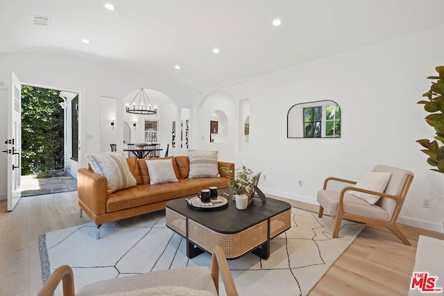 living room featuring lofted ceiling, a chandelier, and light hardwood / wood-style flooring