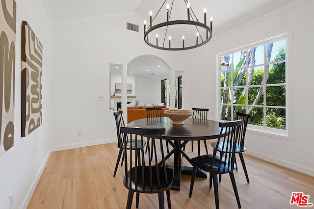 dining area with an inviting chandelier, ornamental molding, vaulted ceiling, and light hardwood / wood-style flooring